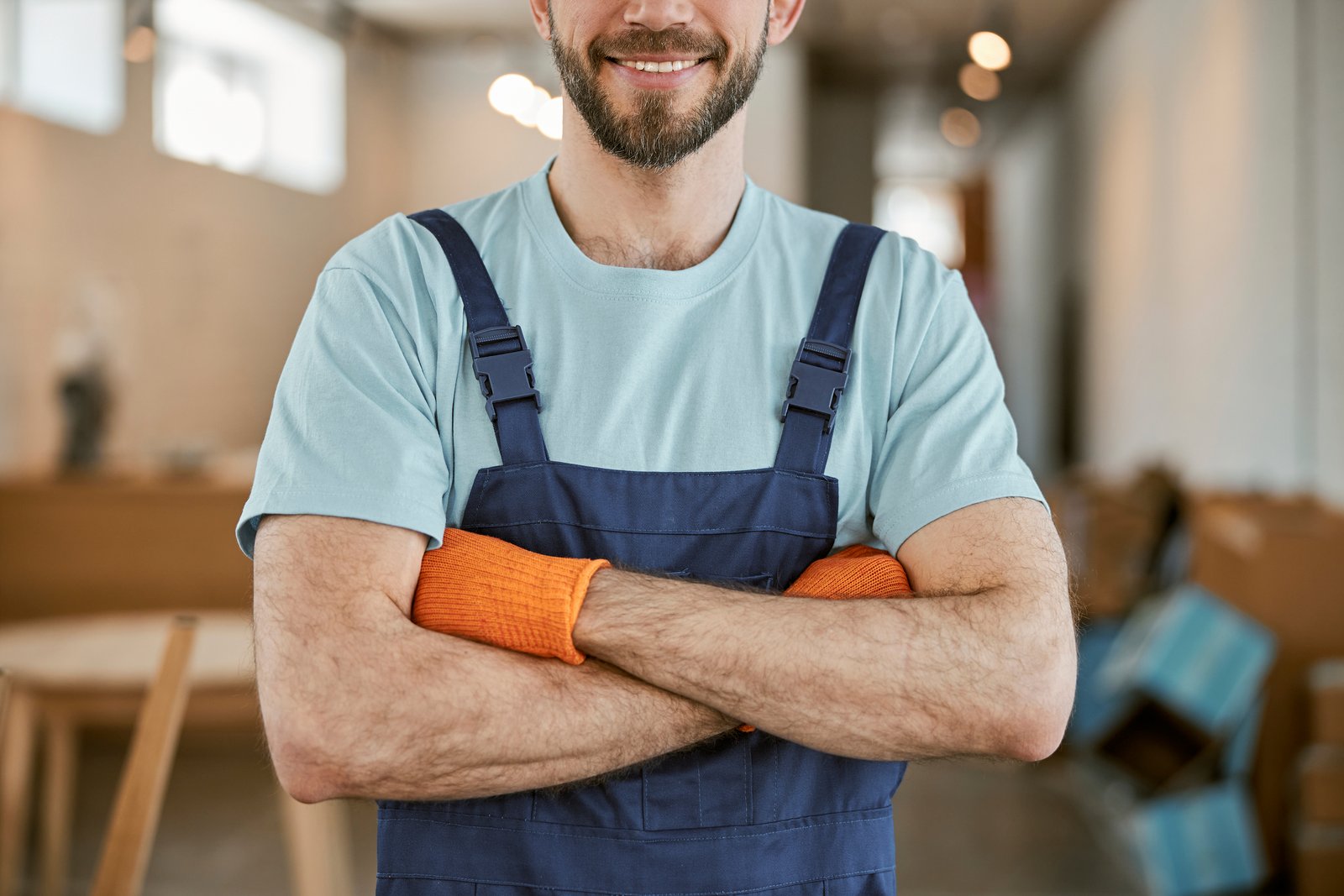 A confident restoration contractor in overalls with arms crossed
